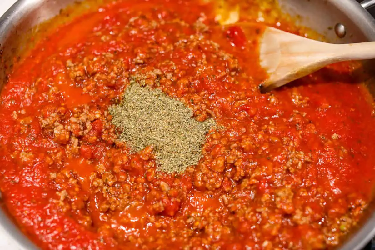 Overhead shot of cooked meat with spaghetti sauce and Italian seasoning added.