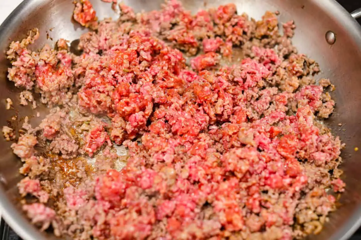 Overhead shot of ground beef and Italian sausage cooking in a skillet. 