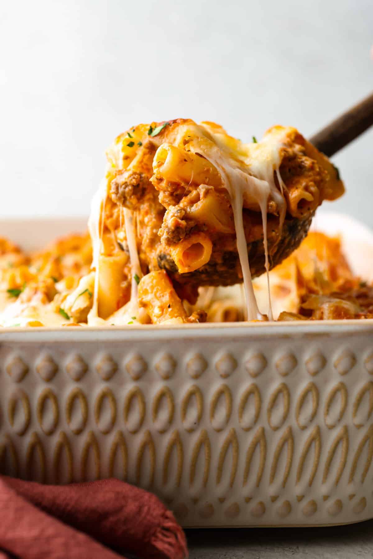 SIde shot of someone scooping a portion of million dollar baked ziti out of the casserole dish. 