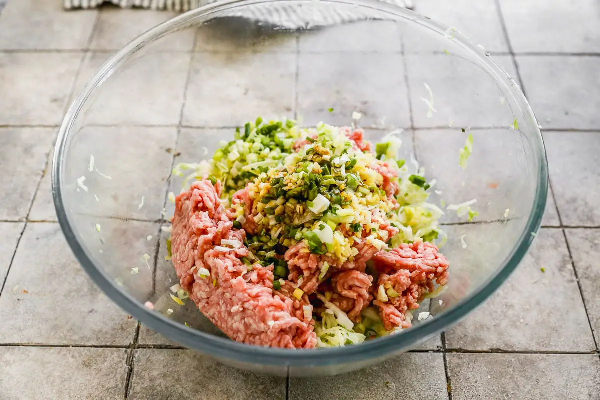 Eine Glasschüssel auf einer gefliesten Arbeitsplatte mit Hackfleisch enthielt mit gehacktem Gemüse wie Zwiebeln und Sellerie.