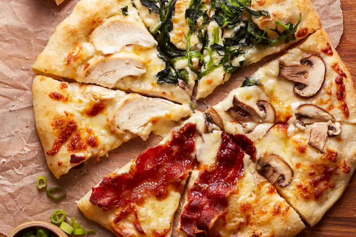 Pizza mit Alfredo-Sauce, mit verschiedenen Belägen auf jeder Scheibe: Hühnchen, Speck, Pilzen und Spinat.