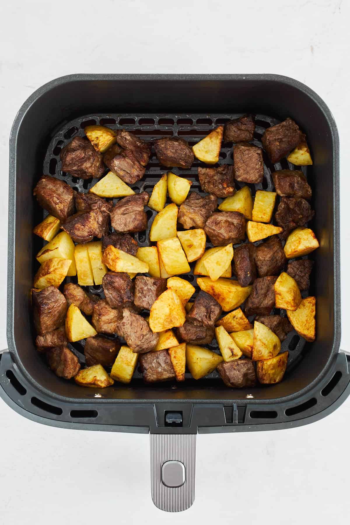 Gekochtes Steak und Kartoffelstücke in einer Heißluftfritteuse. 