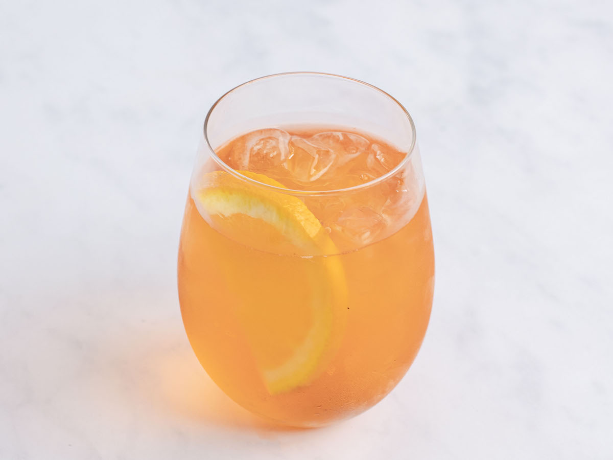 Aperol Spritz im großen Weinglas mit Eiswürfeln und Orangengarnitur