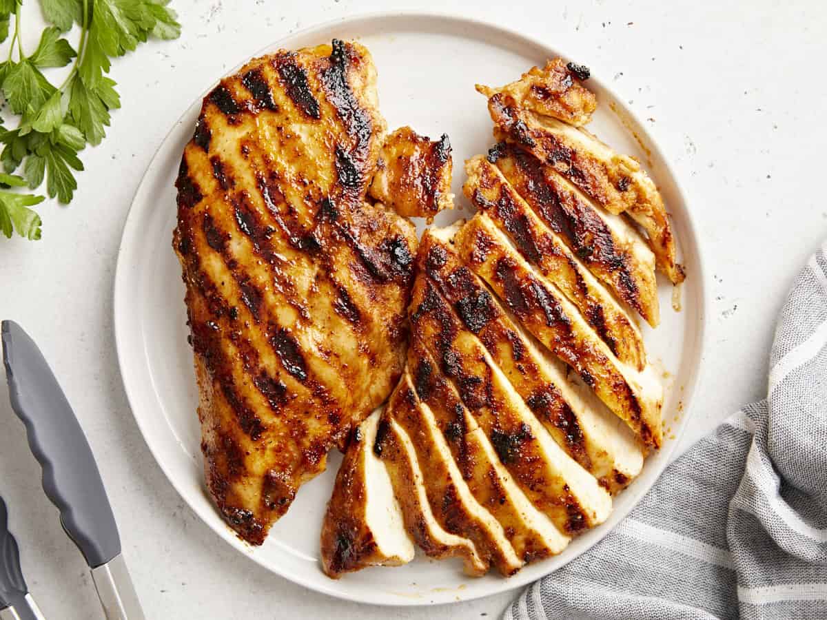 overhead view of 2 sliced grilled chicken breasts on a white plate.