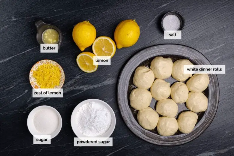 Draufsicht der Zutaten für die einfache Zubereitung von Zitronenrollen auf einer dunklen Oberfläche.