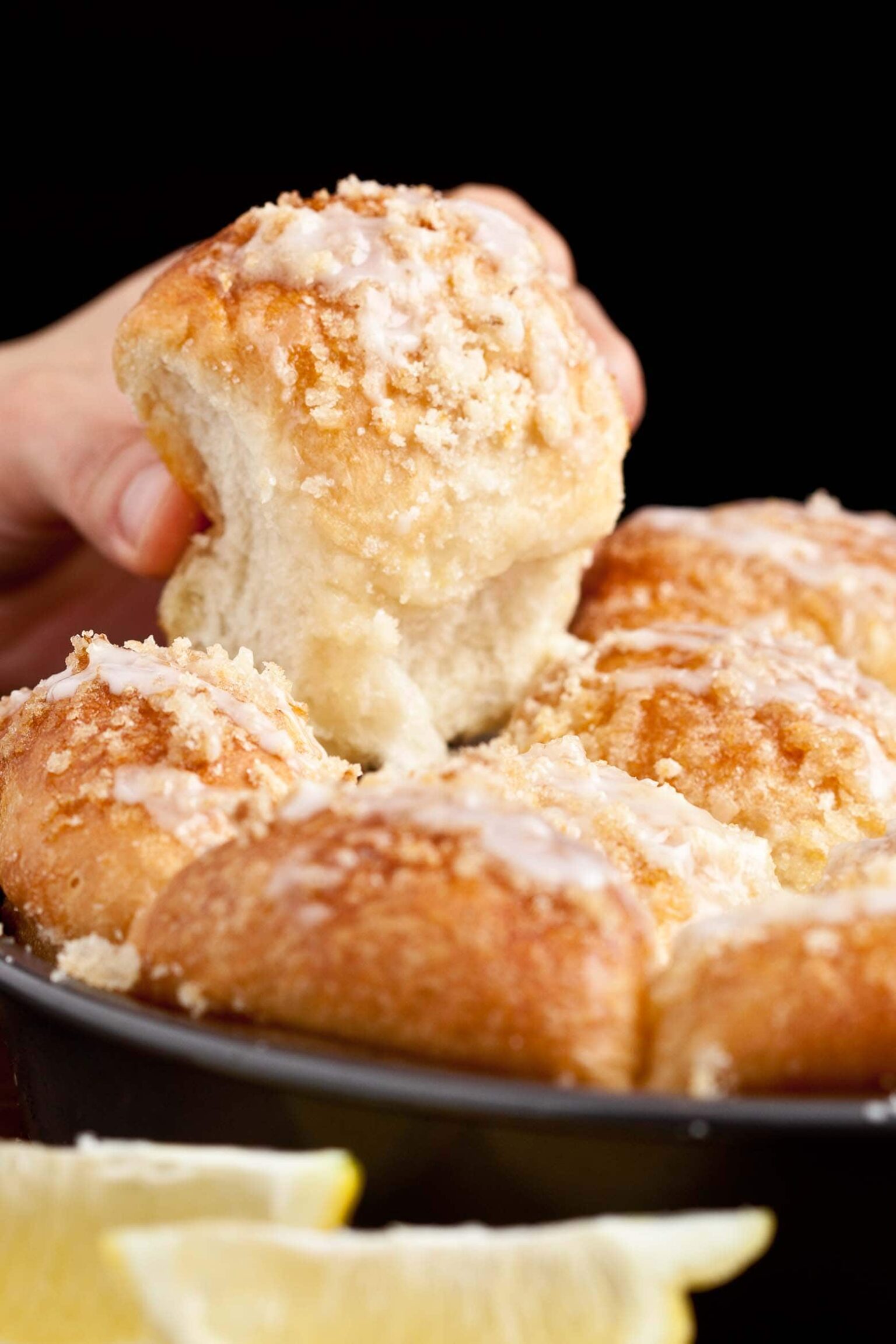 A hand pulling a piece of easy lemon rolls from a pan, topped with icing and crunchy topping.