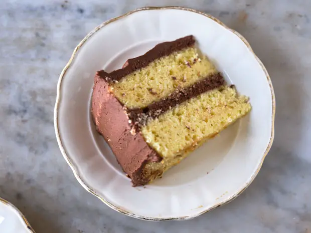 ein Stück klassischen gelben Kuchen mit Schokoladenglasur auf einem Teller gehalten