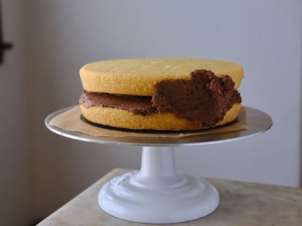 einen gelben Kuchen auf einem Kuchenständer mit Schokoladenglasur bestreichen
