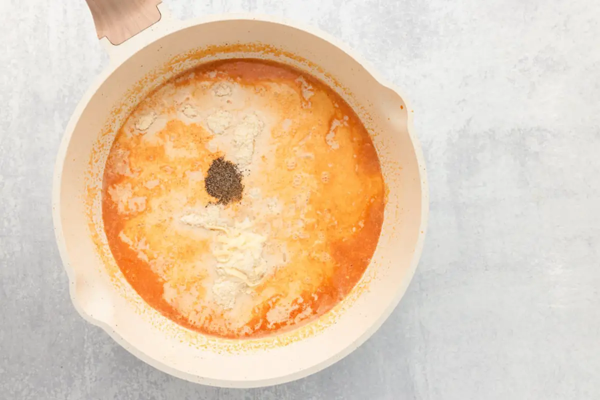 Geriebener Parmesankäse und geriebener Mozzarellakäse in die Pfanne geben