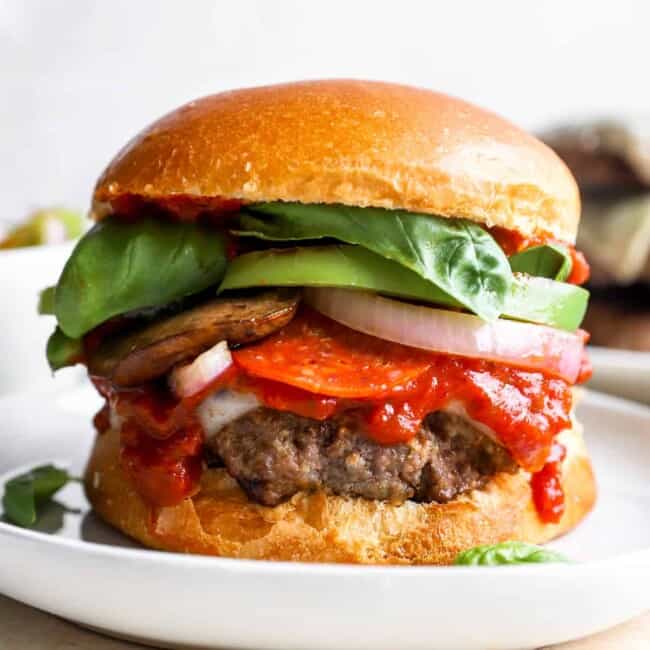 ein Burger auf einem Teller mit Tomaten, Salat und anderen Belägen.