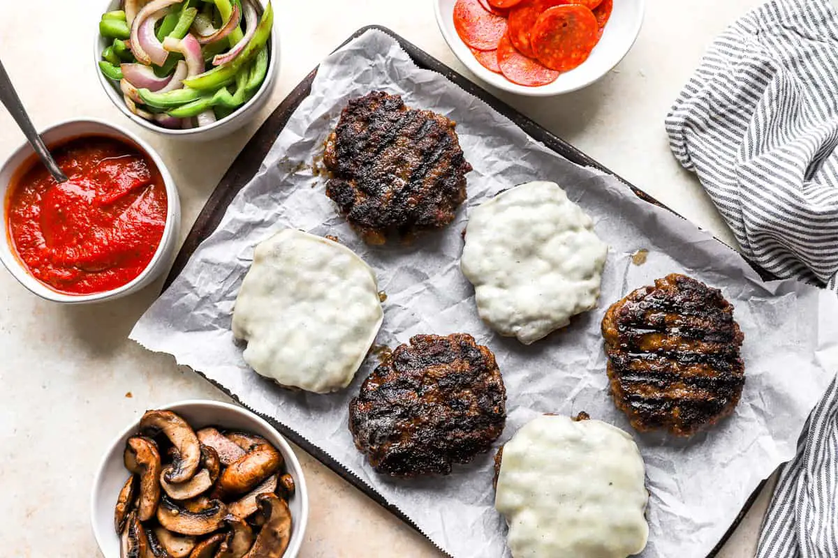 gegrillte Burger mit Sauce und Gemüse auf einem Backblech.