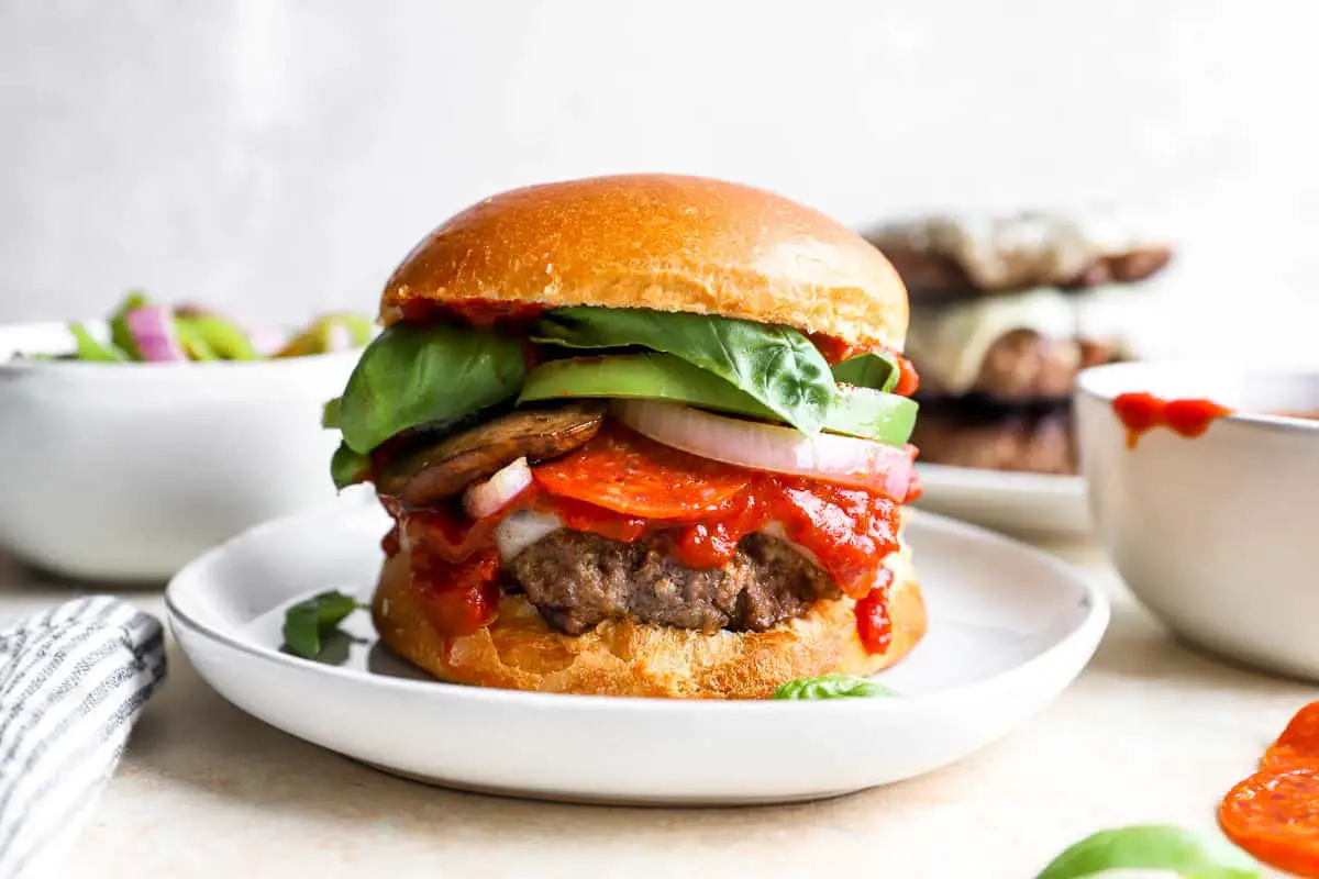 ein Burger auf einem Teller mit Tomaten und Basilikum.