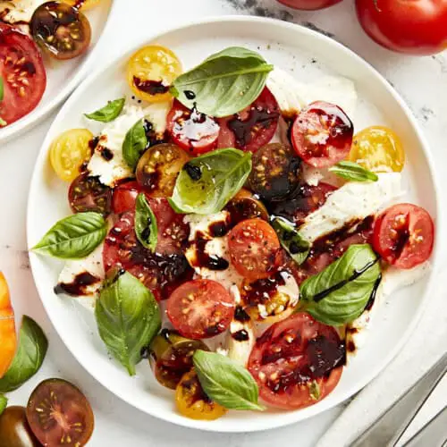 Draufsicht auf eine Portion Caprese-Salat auf einem weißen Teller mit Balsamico-Glasur.