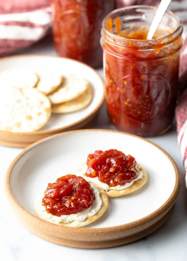 Zwei Cracker auf einem Teller mit Käse und Tomatenmarmelade.