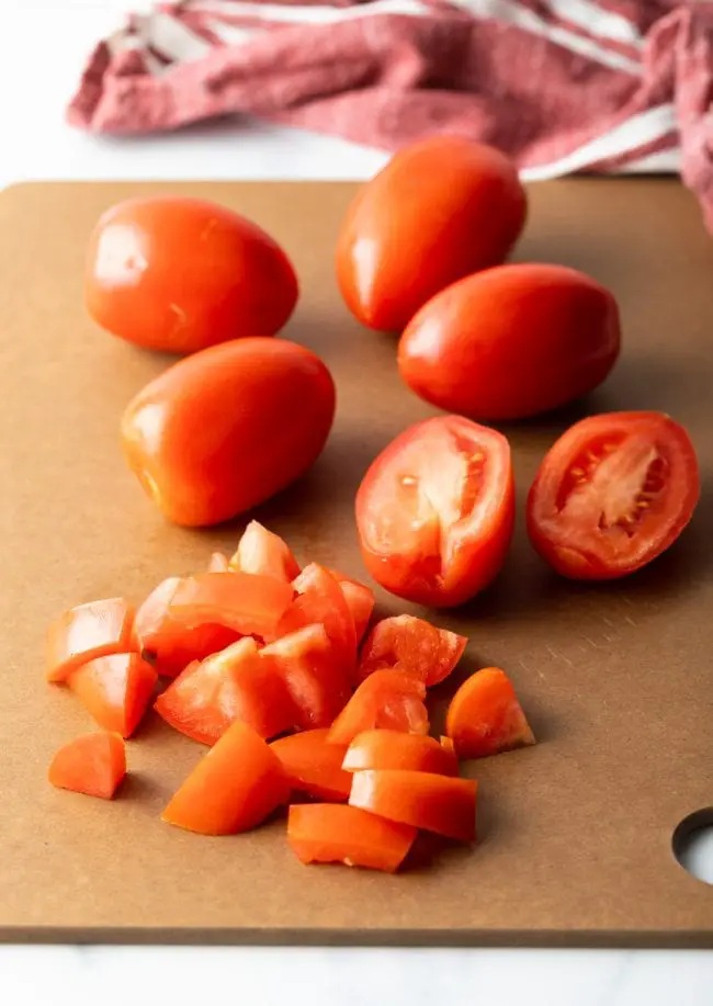 Tomaten werden auf einem Schneidebrett in Stücke geschnitten. 