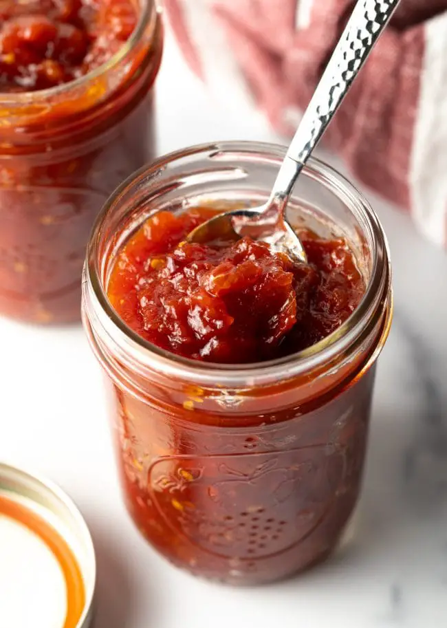 Einen Löffel Tomatenmarmelade aus einem Einmachglas löffeln.