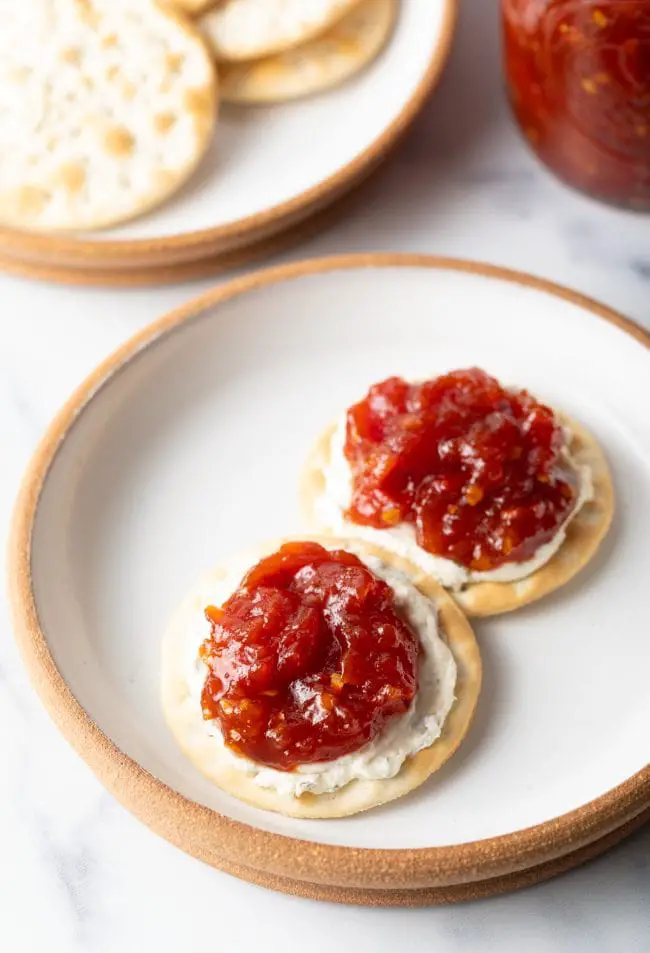 Draufsicht auf einen Teller mit zwei Crackern, Käse und einem Klecks dieses Tomatenmarmeladenrezepts.