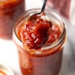 Tomato jam in a jar with a spoon scooping up some jam.