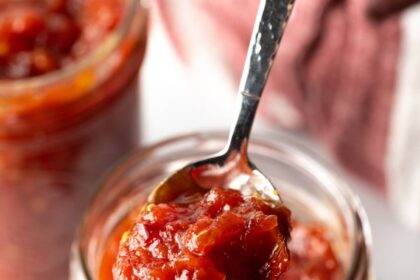 Tomato jam in a jar with a spoon scooping up some jam.