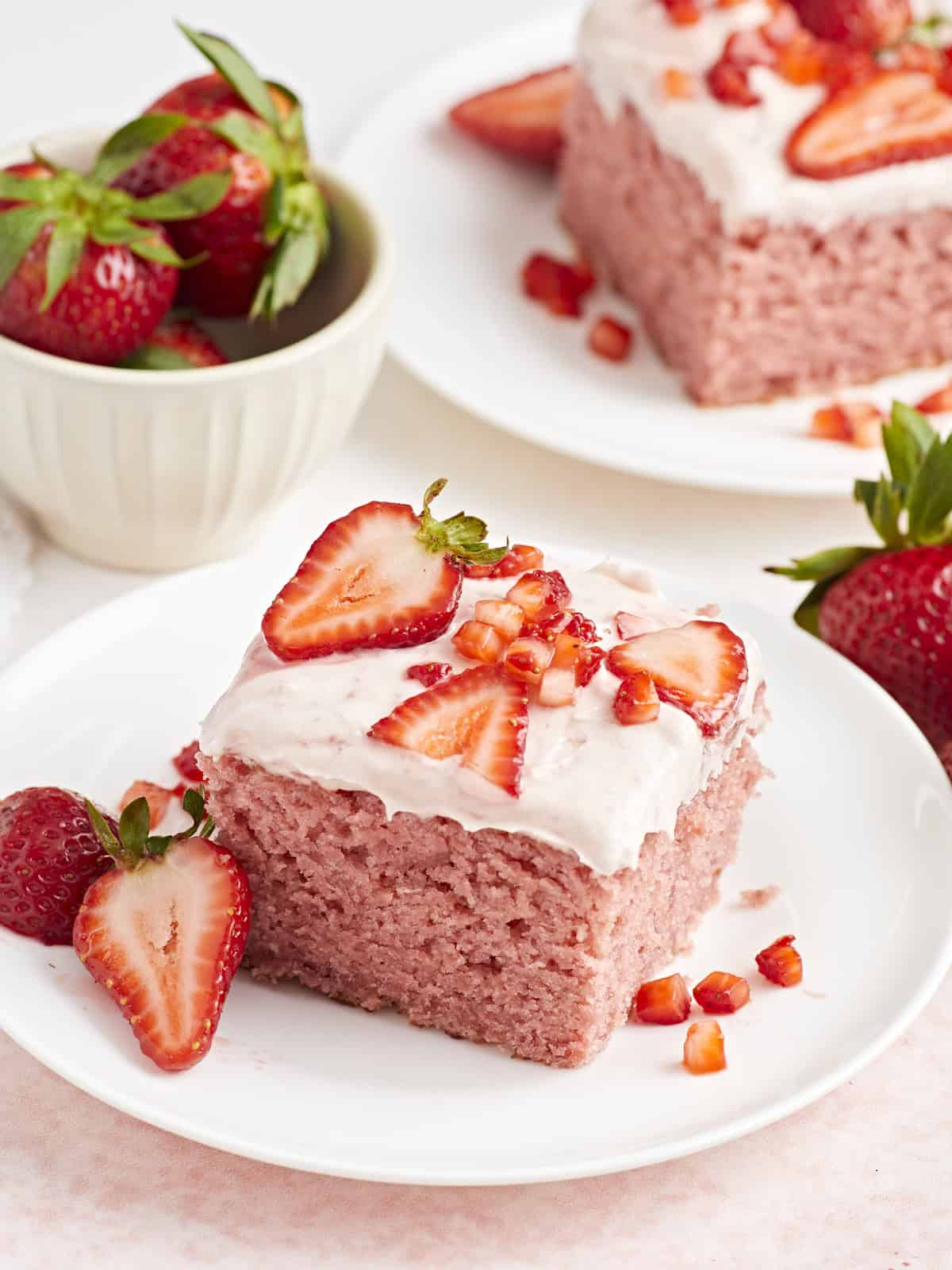 Seitenansicht eines Stücks Erdbeerblechkuchen auf einem kleinen weißen Teller mit frischen Erdbeeren an der Seite.