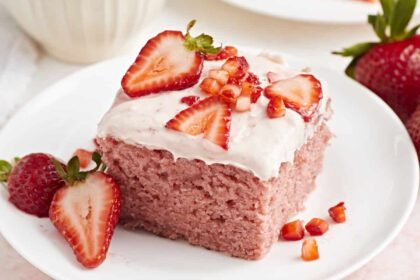 Close up view of strawberry sheet cake on a white plate with fresh strawberries on top.