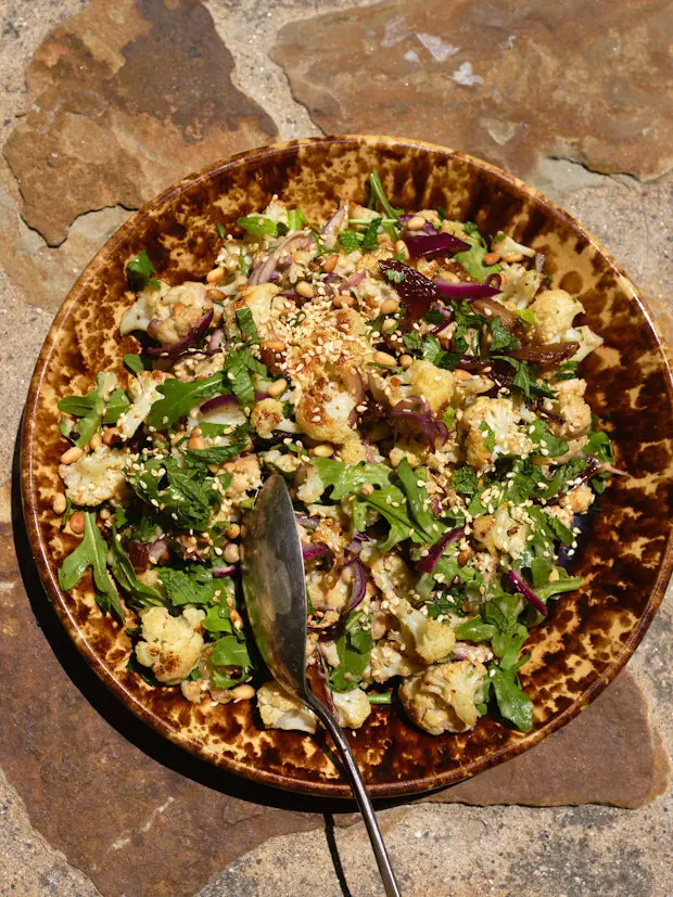 gerösteter Blumenkohl auf einer Platte mit Tahini-Glasur, Minze, Kräutern, Datteln und mehr