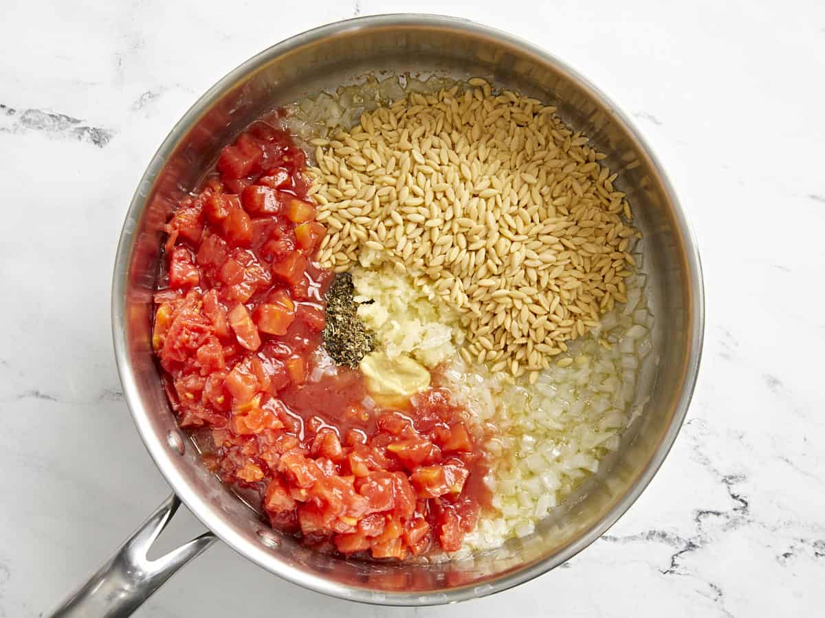 Tomaten und Orzo werden zu den in einer Pfanne sautierten Zwiebeln gegeben.