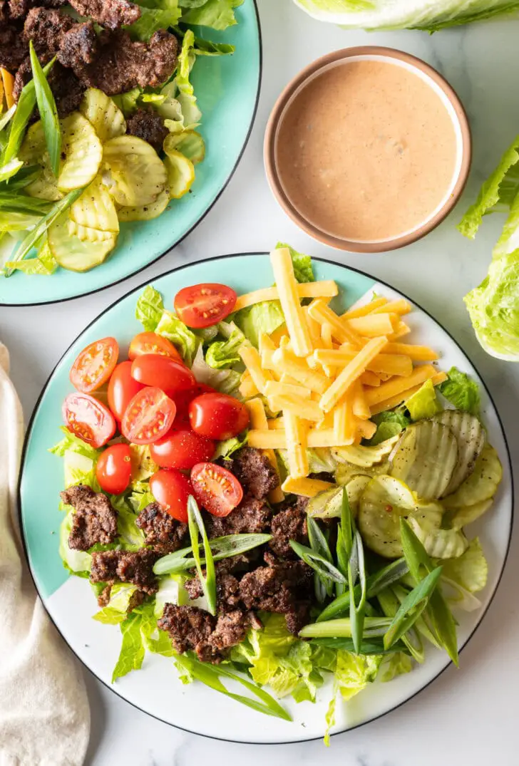 Reichhaltiger Big-Mac-Cheeseburger-Salat mit geraspeltem Salat, Hackfleisch, halbierten Kirschtomaten, geriebenem Käse, Gurken und geschnittenen Frühlingszwiebeln.