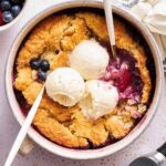 A bowl of mixed berry cobbler topped with three scoops of vanilla ice cream.