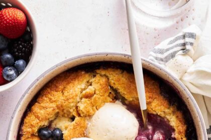 A bowl of mixed berry cobbler topped with three scoops of vanilla ice cream.