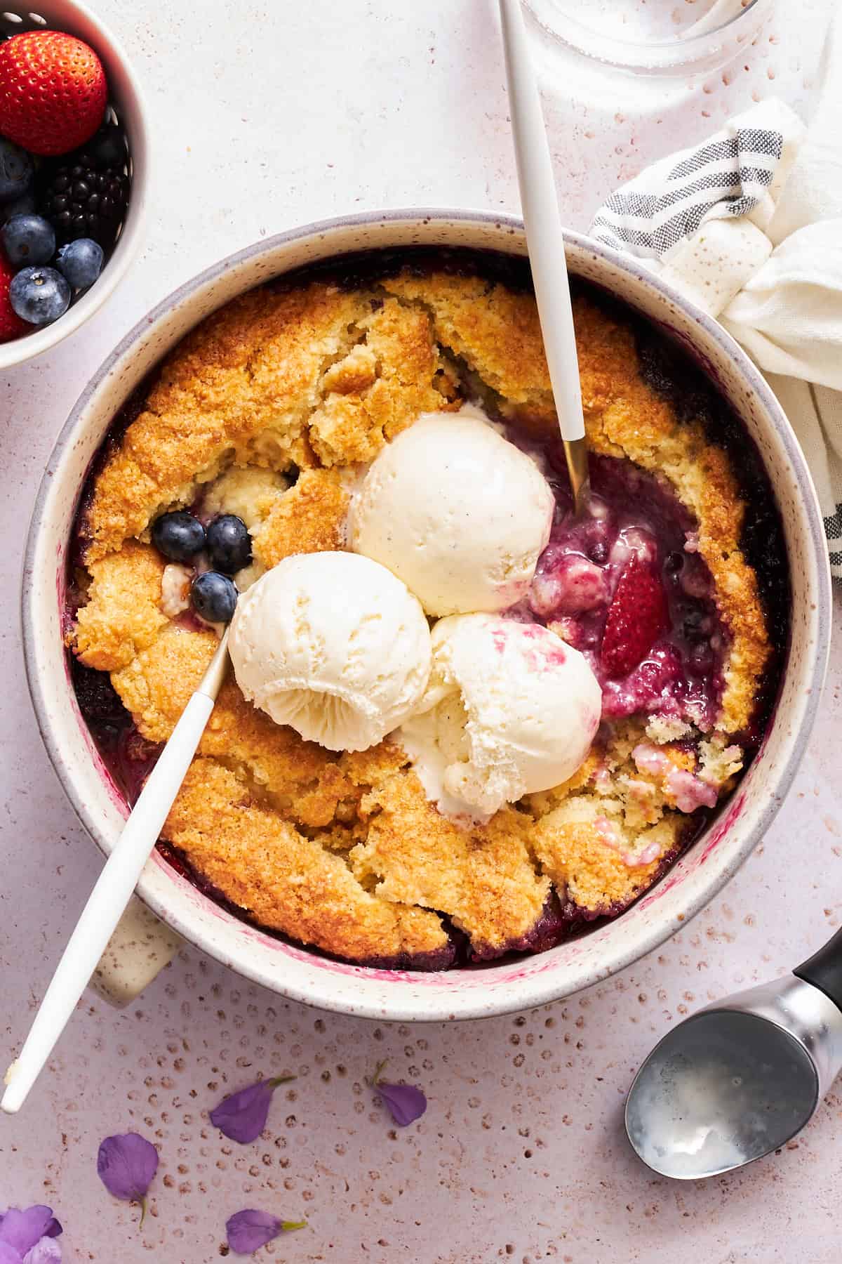 A bowl of mixed berry cobbler topped with three scoops of vanilla ice cream.