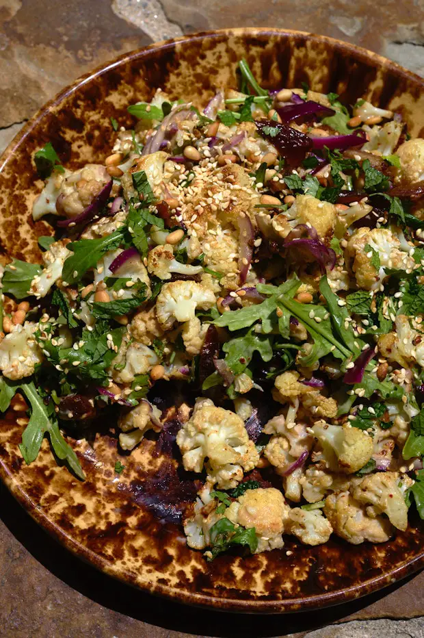 gerösteter Blumenkohl auf einer Platte mit Tahini-Glasur, Minze, Kräutern, Datteln und mehr