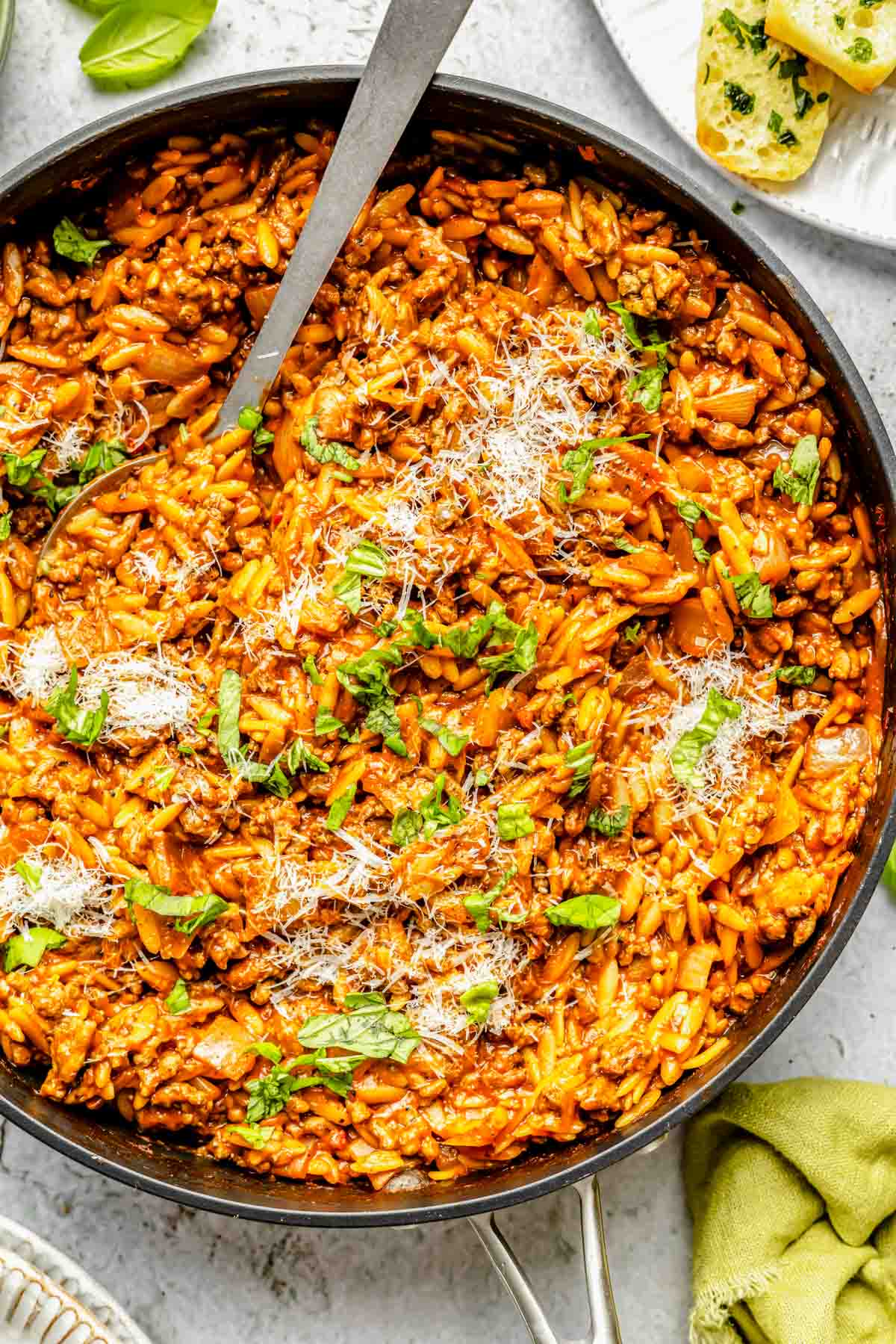 ground beef and orzo in a large nonstick skillet garnished with fresh basil leaves and grated parmesan cheese with a metal spoon