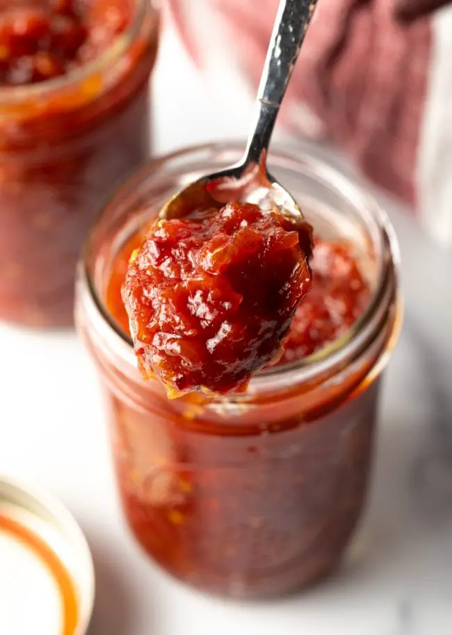 Tomatenmarmelade in einem Glas, mit einem Löffel wird etwas Marmelade herausgenommen. 