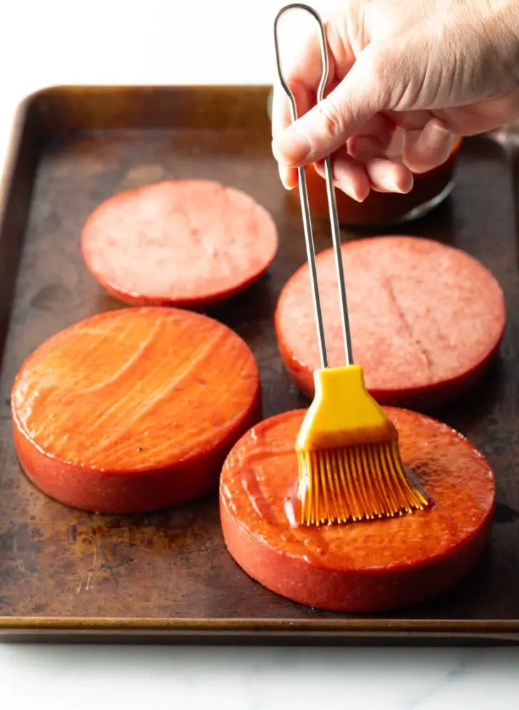 Bestreichen Sie 4 dicke Scheiben Wurst mit Barbecuesoße von Hand und verwenden Sie dazu einen gelben Backpinsel.