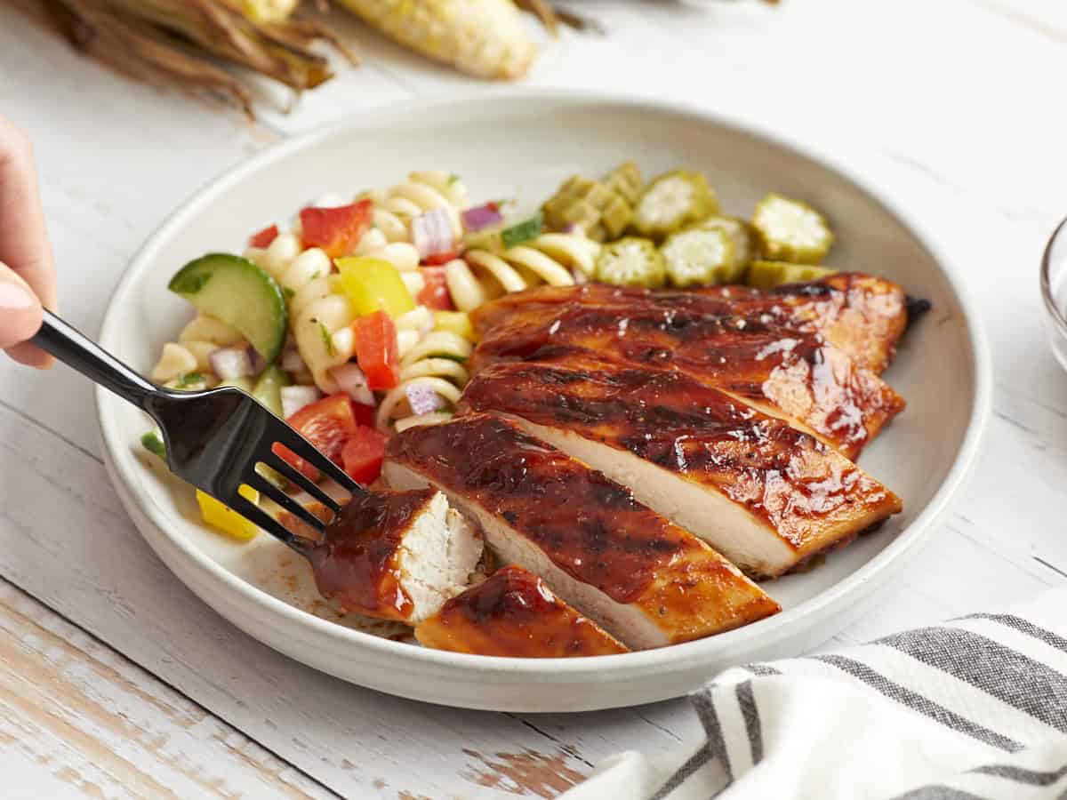 eine Portion gegrilltes Hähnchen in Scheiben auf einem weißen Teller mit Nudelsalat und Okra.