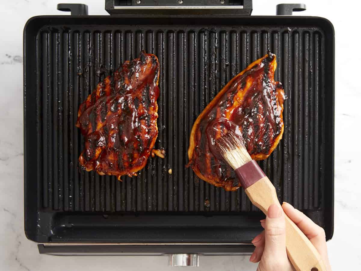 Gegrillte Hähnchenbrüste auf einem Indoor-Grill mit Barbecuesauce bestreichen.