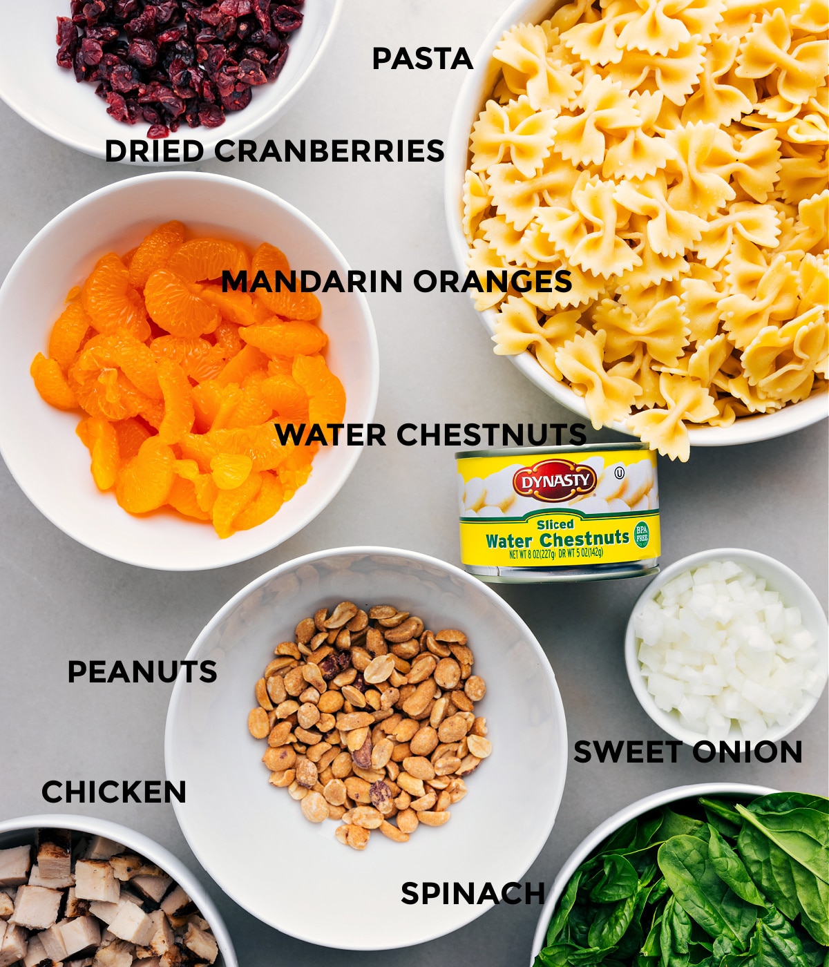 Zutaten wie getrocknete Preiselbeeren, Nudeln, Wasserkastanien, Orangen, Zwiebeln, Spinat, Erdnüsse und Hühnchen sind für eine einfache Zubereitung vorbereitet.