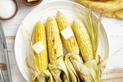 overhead view of 4 peeled ears of grilled corn with butter on a white plate.