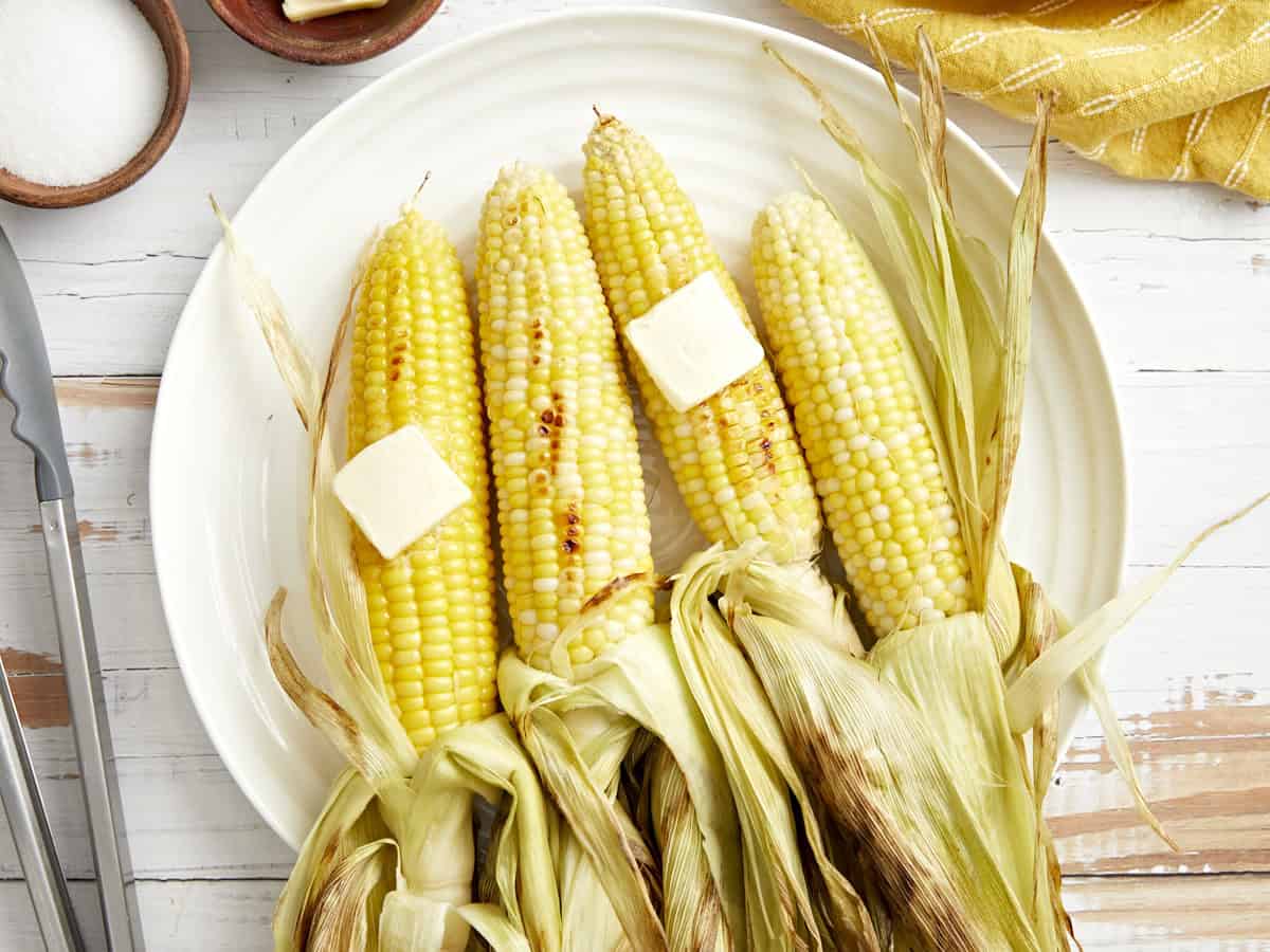 overhead view of 4 peeled ears of grilled corn with butter on a white plate.