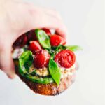 A piece of cottage cheese toast being held up showing all the yummy toppings.