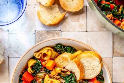 a bowl with a metal spoon has sausage tortellini soup and sliced bread on the inside
