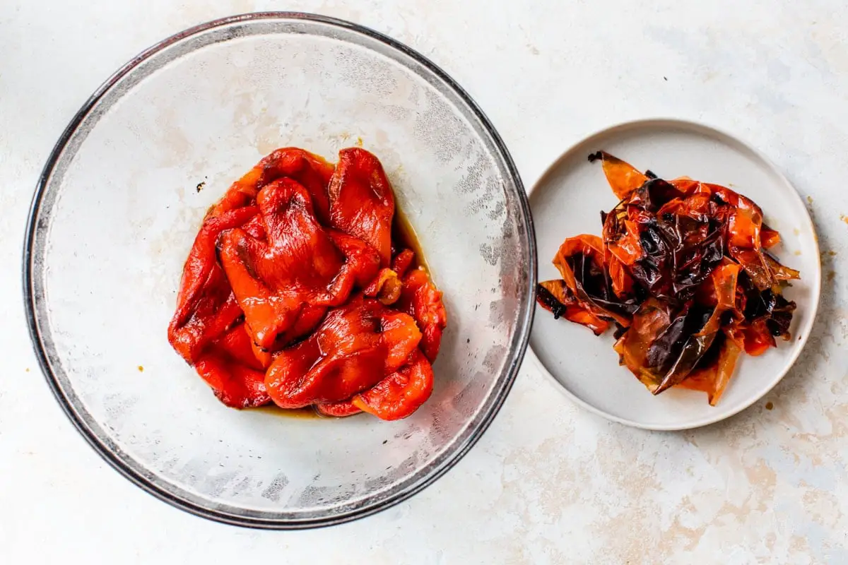 Geröstete rote Paprika in einer Schüssel neben entfernten verkohlten Schalen