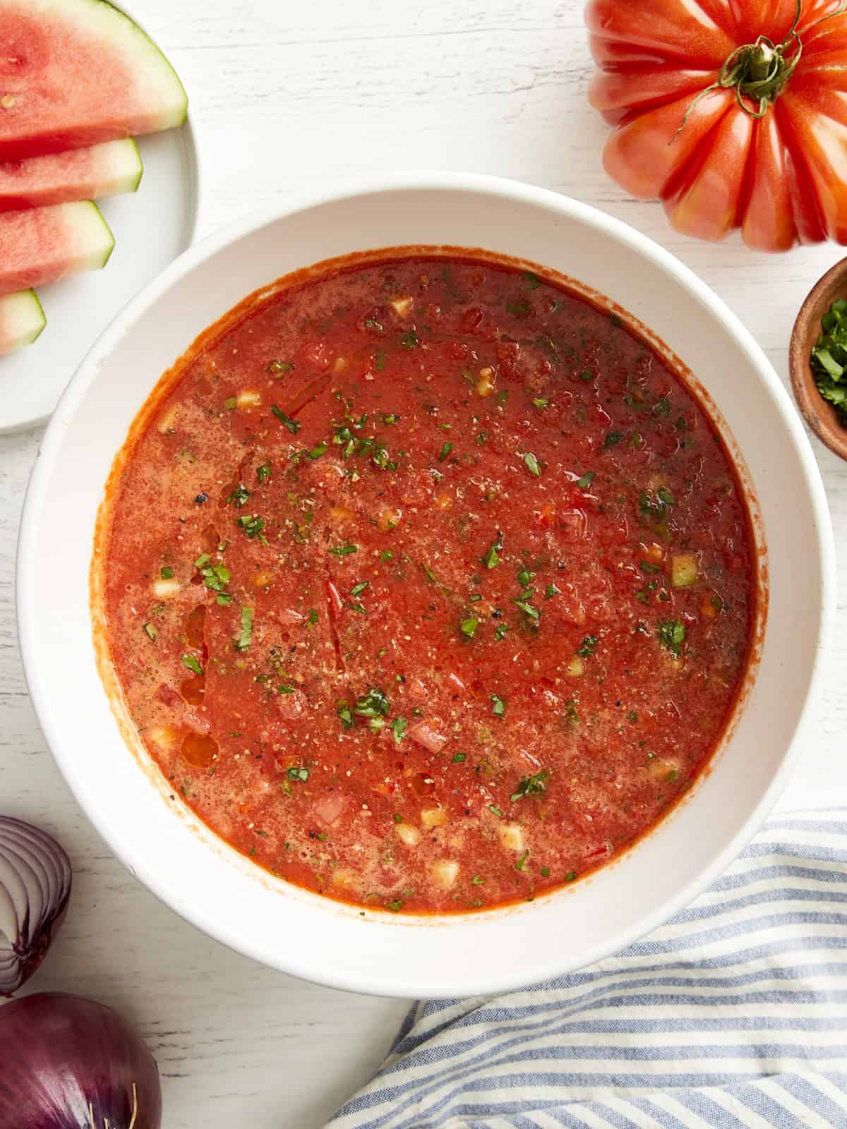 Draufsicht auf Wassermelonen-Gazpacho in einer weißen Schüssel mit gehackten frischen Kräutern.