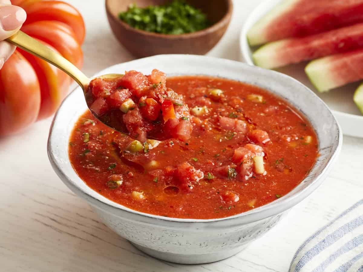 Ein Löffel schöpft einen Bissen Wassermelonen-Gazpacho aus einer weißen Schüssel.