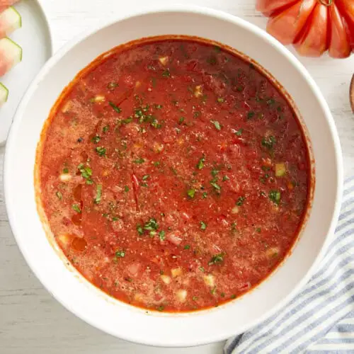 Draufsicht auf Wassermelonen-Gazpacho in einer weißen Schüssel mit gehackten frischen Kräutern.