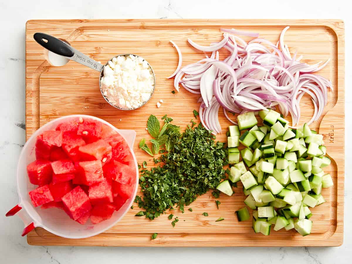 Mise en Place für Wassermelonen-Feta-Salat auf einem Holzschneidebrett.