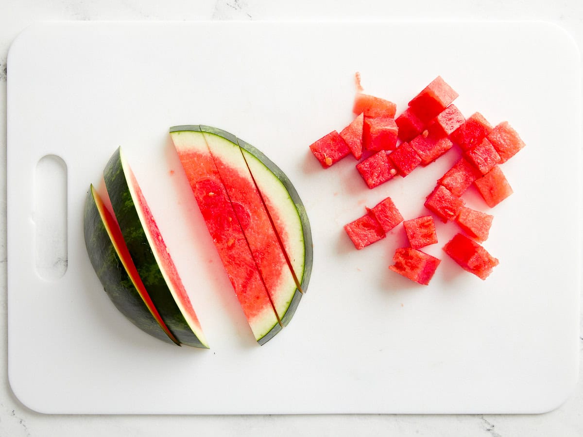 teilweise gewürfelte Wassermelone auf einem weißen Schneidebrett.