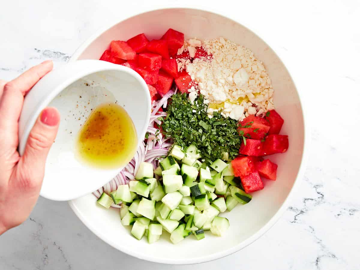 Dressing über Wassermelonen-Feta-Salat in einer weißen Schüssel gießen.