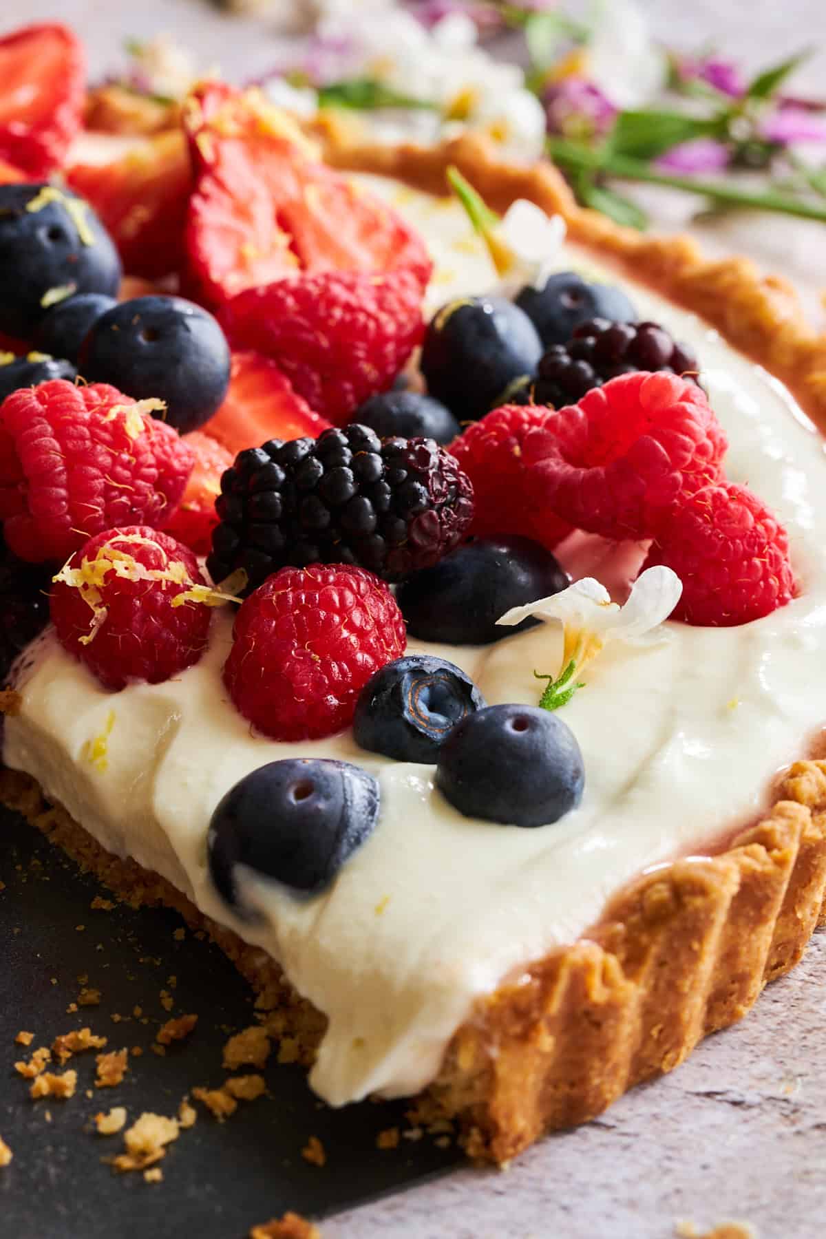 Seitenansicht einer Käsekuchen-Obst-Tarte, belegt mit frischen Himbeeren, Brombeeren und Blaubeeren. 